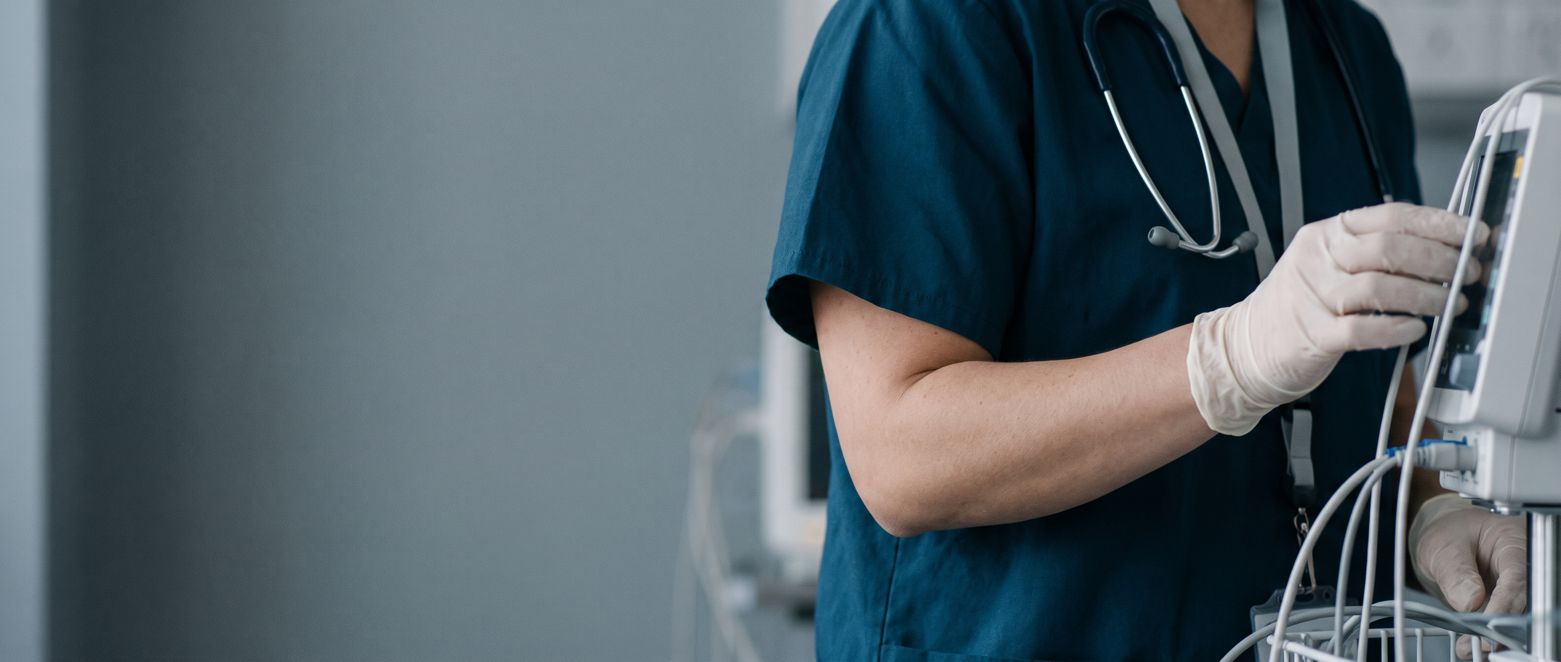 Allied health professional in deep teal scrubs adjusting clinical equipment