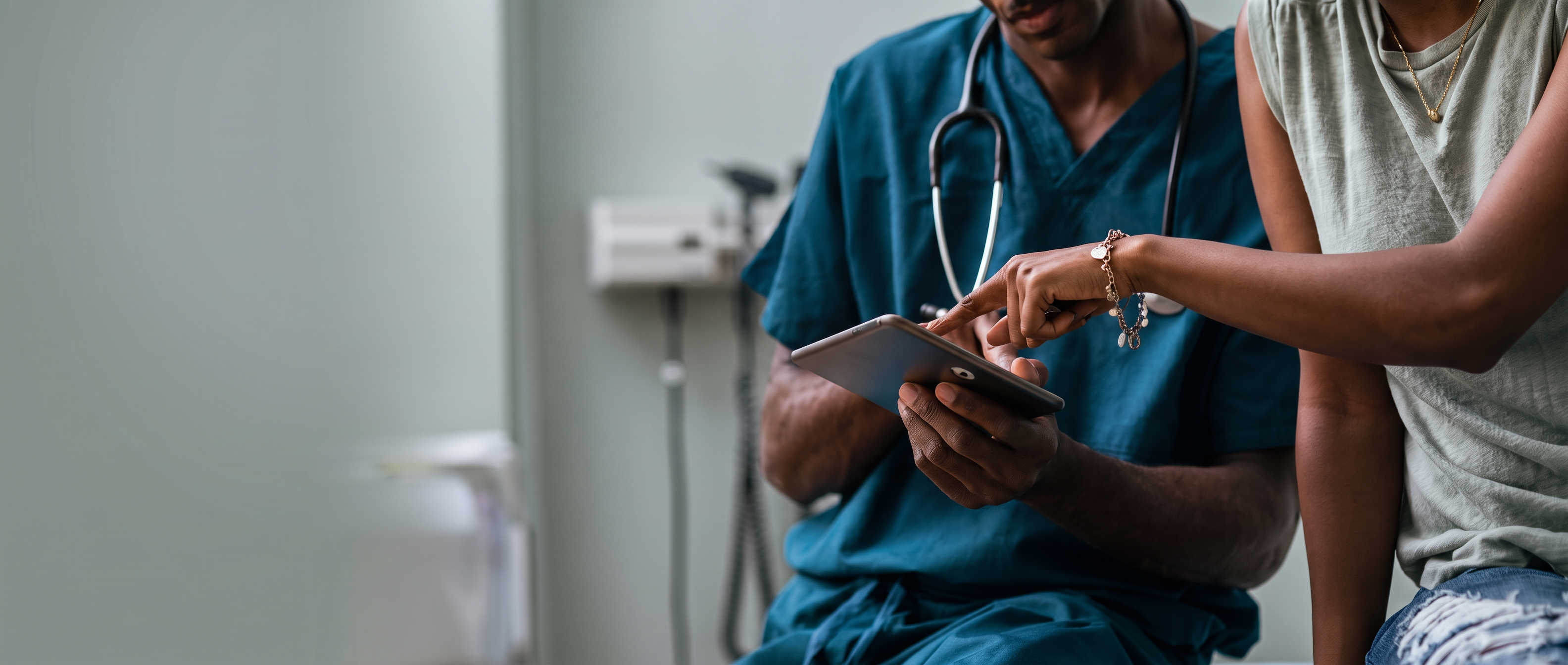 Clinician in scrubs reviewing a chart on a tablet with a patient